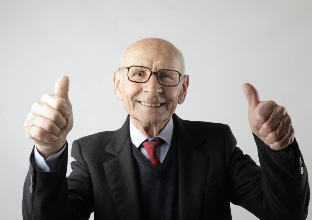 Cheerful elderly man in suit giving thumbs up, symbolizing success and approval.